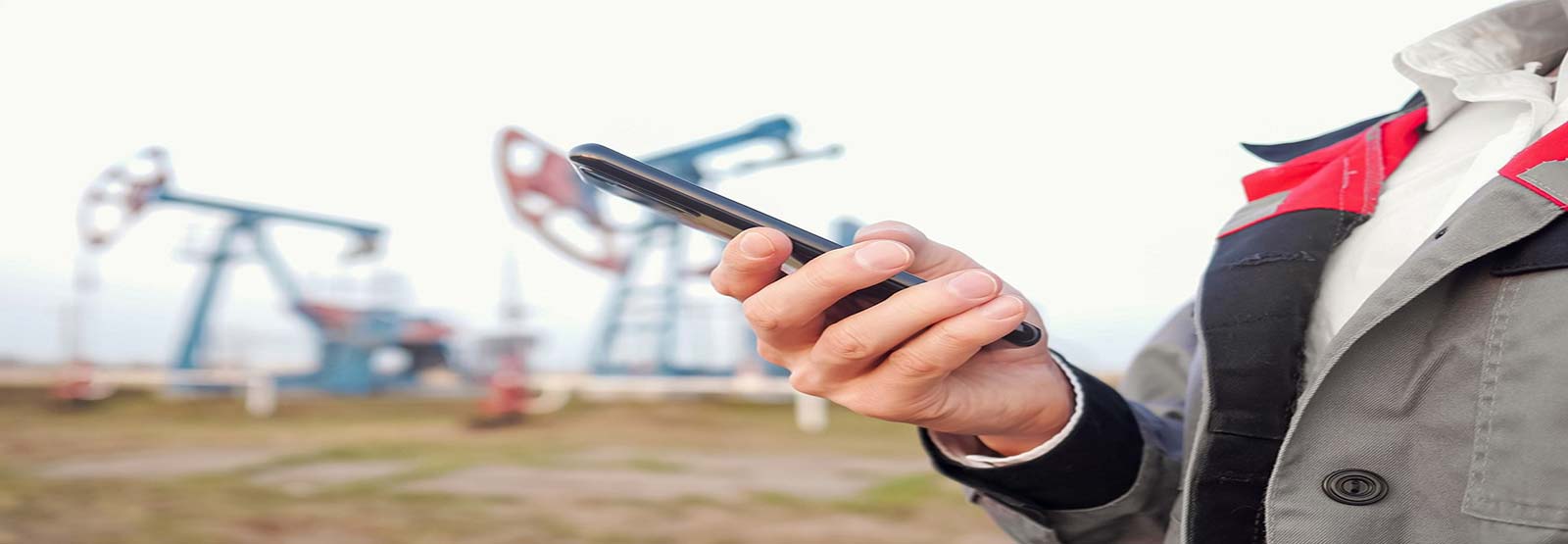 Person holding smart phone with oil rigs in background.