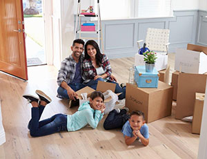 Family on floor of new home around moving boxes smiling together.