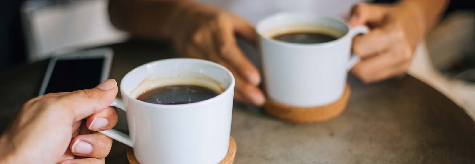 Two people holding coffee cups with mobile phone on table.